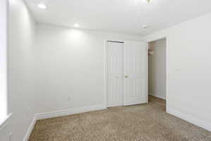 Carpeted room featuring white walls, white trim, recessed lighting, and a closet with bifold doors