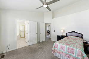 Vaulted ceiling bedroom featuring carpeting, a ceiling fan, and access to an en-suite bathroom with a built-in tub and glass-enclosed shower