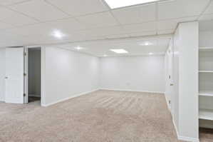 Spacious room featuring neutral carpeting, a drop-tile ceiling with recessed lighting and a flush-mount fixture, built-in shelving, and white interior doors