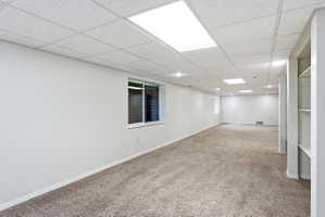 Spacious finished basement featuring recessed lighting, drop ceiling, light brown carpet, a horizontal window, and built-in shelving