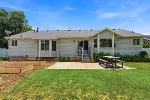 Rear exterior with light gray siding, featuring a concrete patio, a sliding glass door with wood steps, a bay window, and several raised garden beds