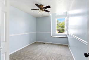 Carpeted room featuring a ceiling fan with light fixture, chair rail molding, and a window with plantation shutters