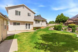 Expansive backyard featuring a manicured lawn, tiered landscaping with mature shrubs, and a concrete patio