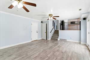 Spacious room featuring wood-finish flooring, two ceiling fans with light fixtures, and white baseboards