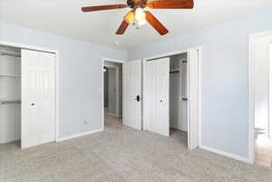 Carpeted room with light blue walls, featuring a ceiling fan with wood-finish blades, two bi-fold closet doors, and painted white trim