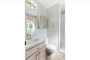Bathroom featuring a vanity with a drop-in sink, an overhead light fixture, a mirrored medicine cabinet, a toilet, and a glass-enclosed shower