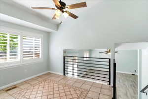 Vaulted ceiling with a ceiling fan, plantation shutters, iron railing, and tile flooring with an inlaid pattern