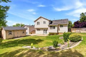 Expansive backyard featuring a manicured lawn, established landscaping, a storage shed, and a privacy fence