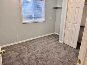 Carpeted room featuring a window with horizontal blinds, light gray walls, white baseboards, and a bi-fold closet door