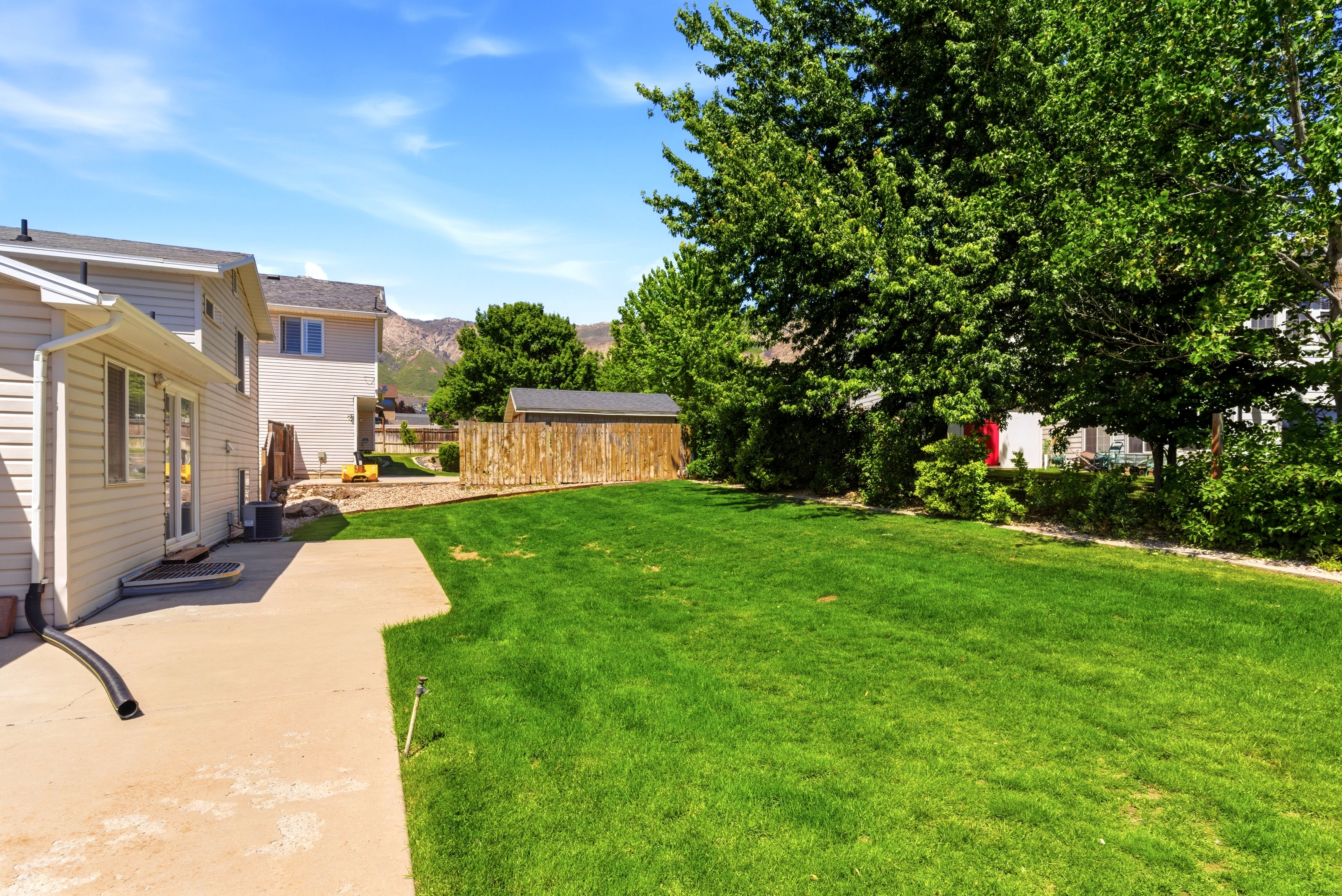 Expansive green lawn with mature trees and a concrete patio