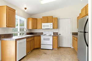 Kitchen featuring light wood cabinetry, white appliances, and composite countertops