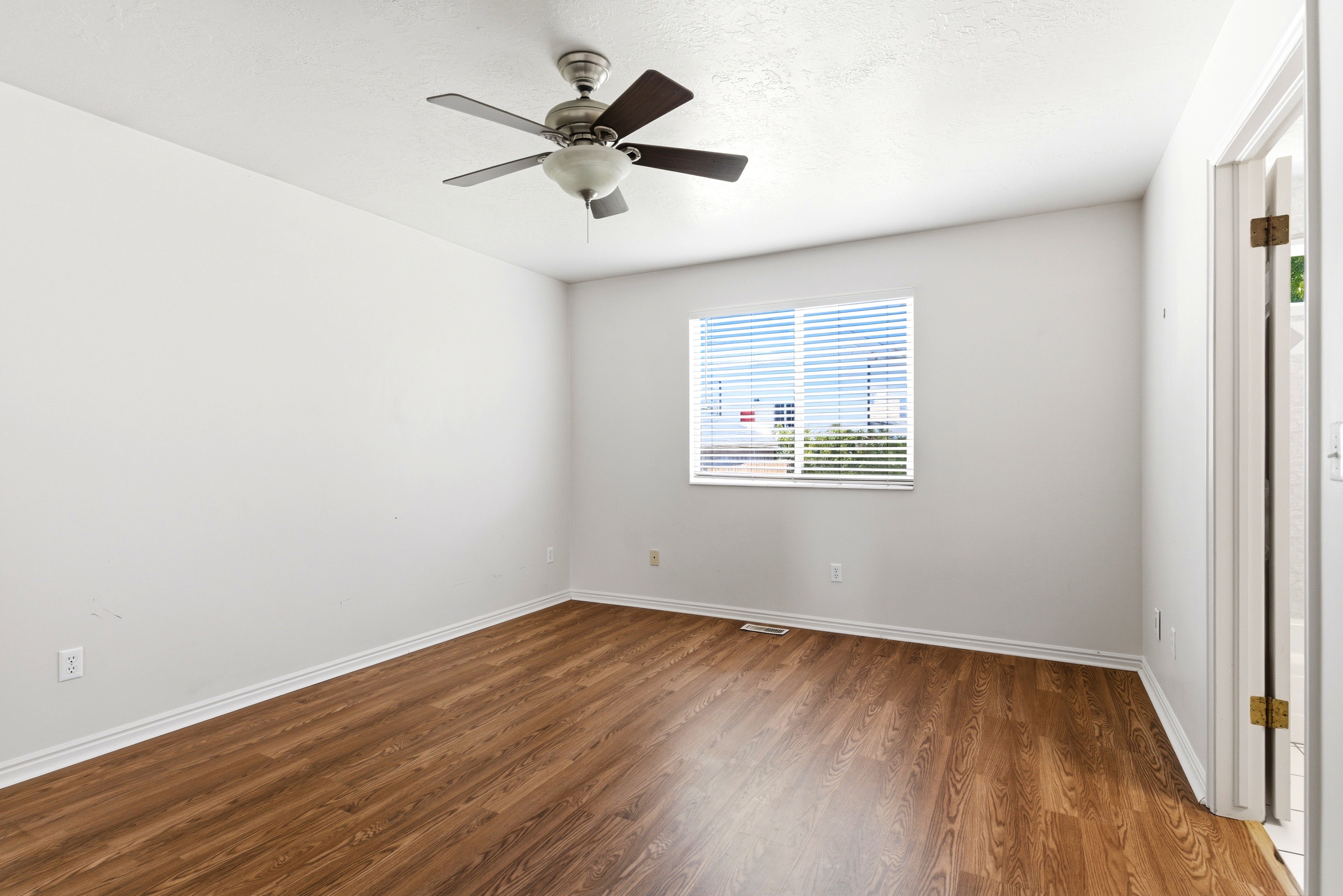 Room featuring wood-finish flooring, white baseboards, a ceiling fan with integrated lighting, a window with horizontal blinds, and a white interior door