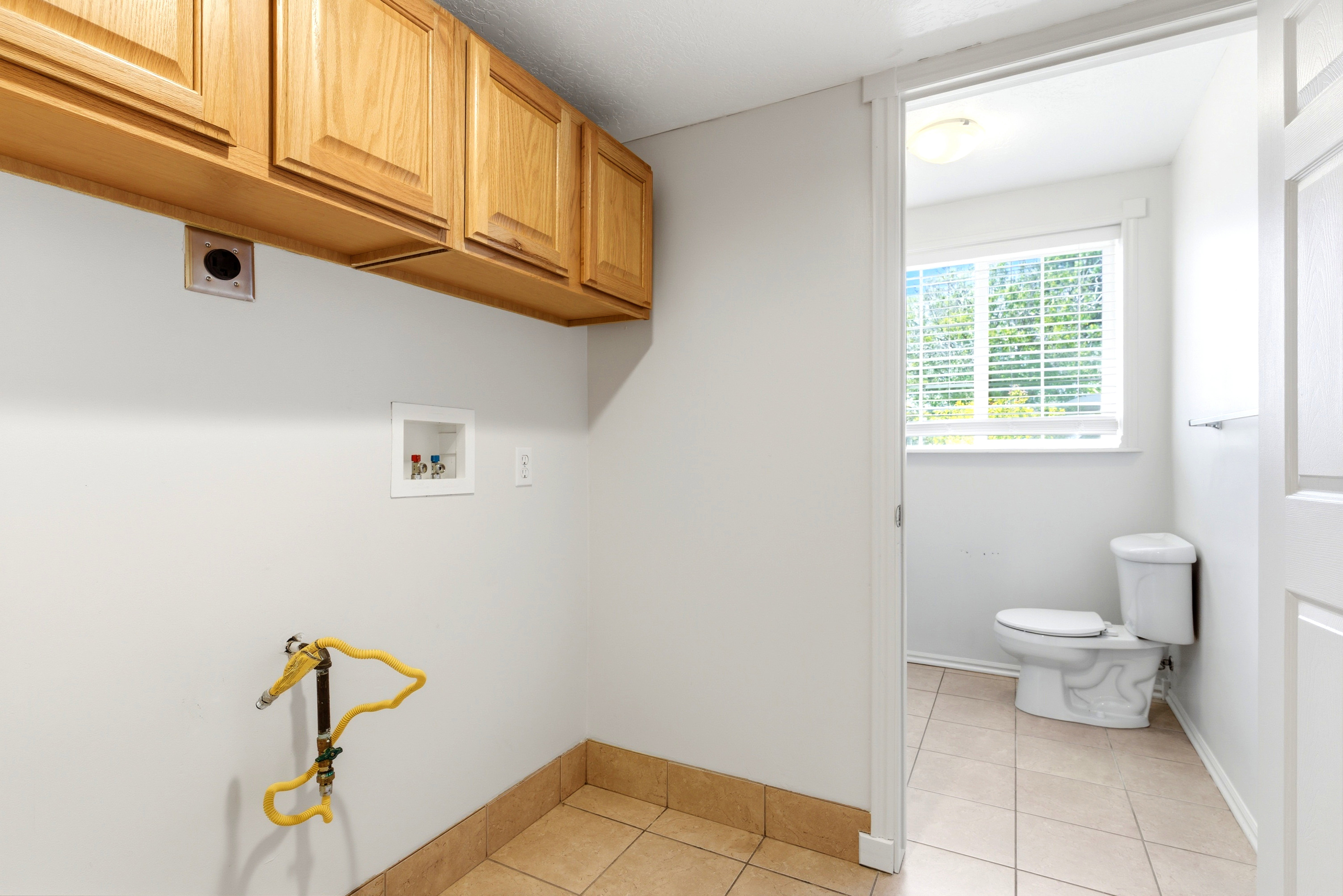 Dedicated laundry area featuring overhead cabinetry, utility connections, and tile flooring