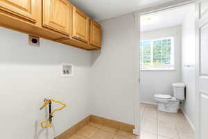 Dedicated laundry area featuring overhead cabinetry, utility connections, and tile flooring