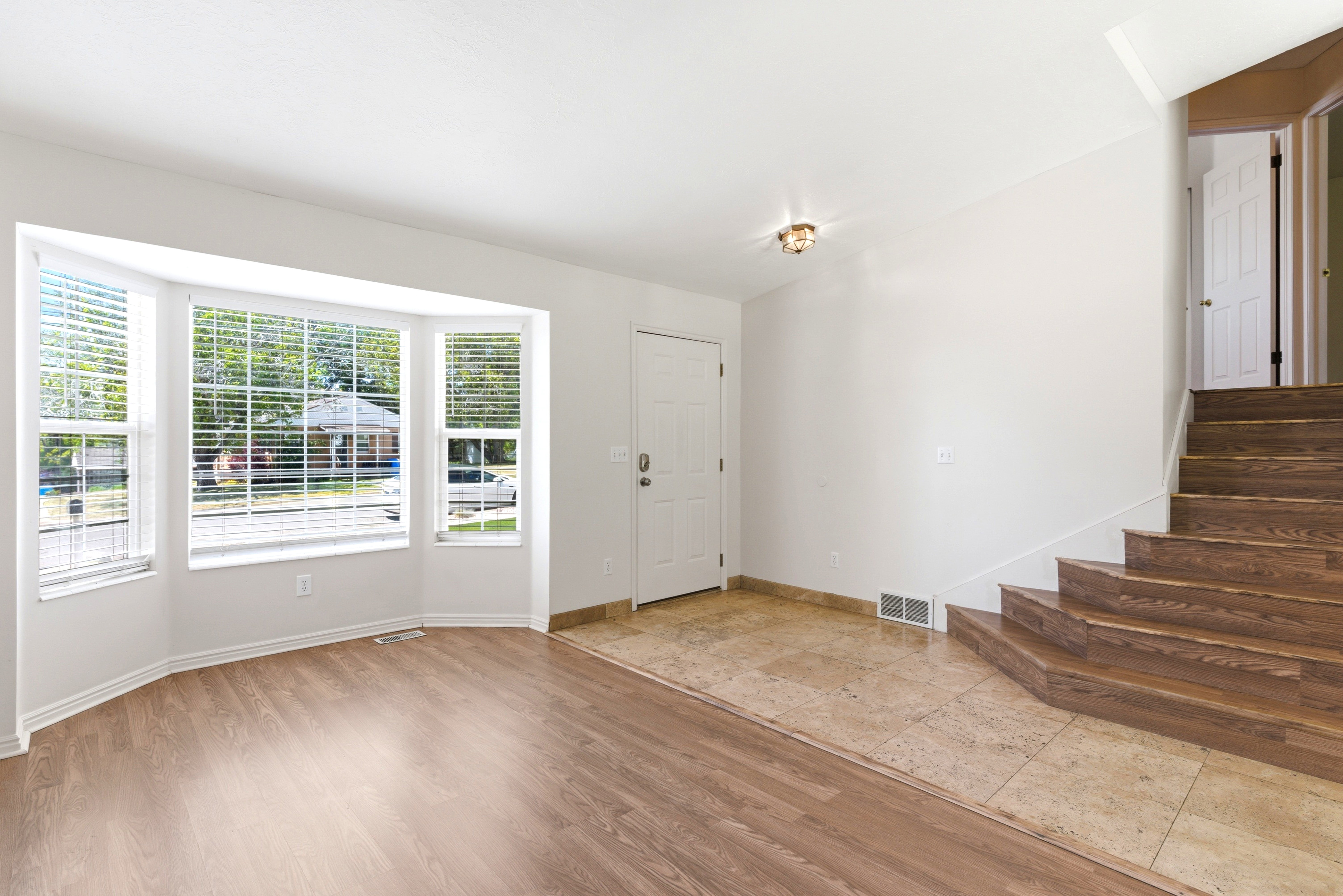 Spacious interior featuring a large bay window with blinds, wood-finish flooring, a tiled entry, and wood stairs