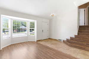 Spacious interior featuring a large bay window with blinds, wood-finish flooring, a tiled entry, and wood stairs
