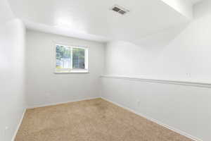 Neutral-toned room featuring light beige carpeting, white walls, and a window with blinds