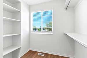 Recessed window with white blinds, wood-finish flooring, built-in shelving, white walls, and a clothing rod with an upper shelf