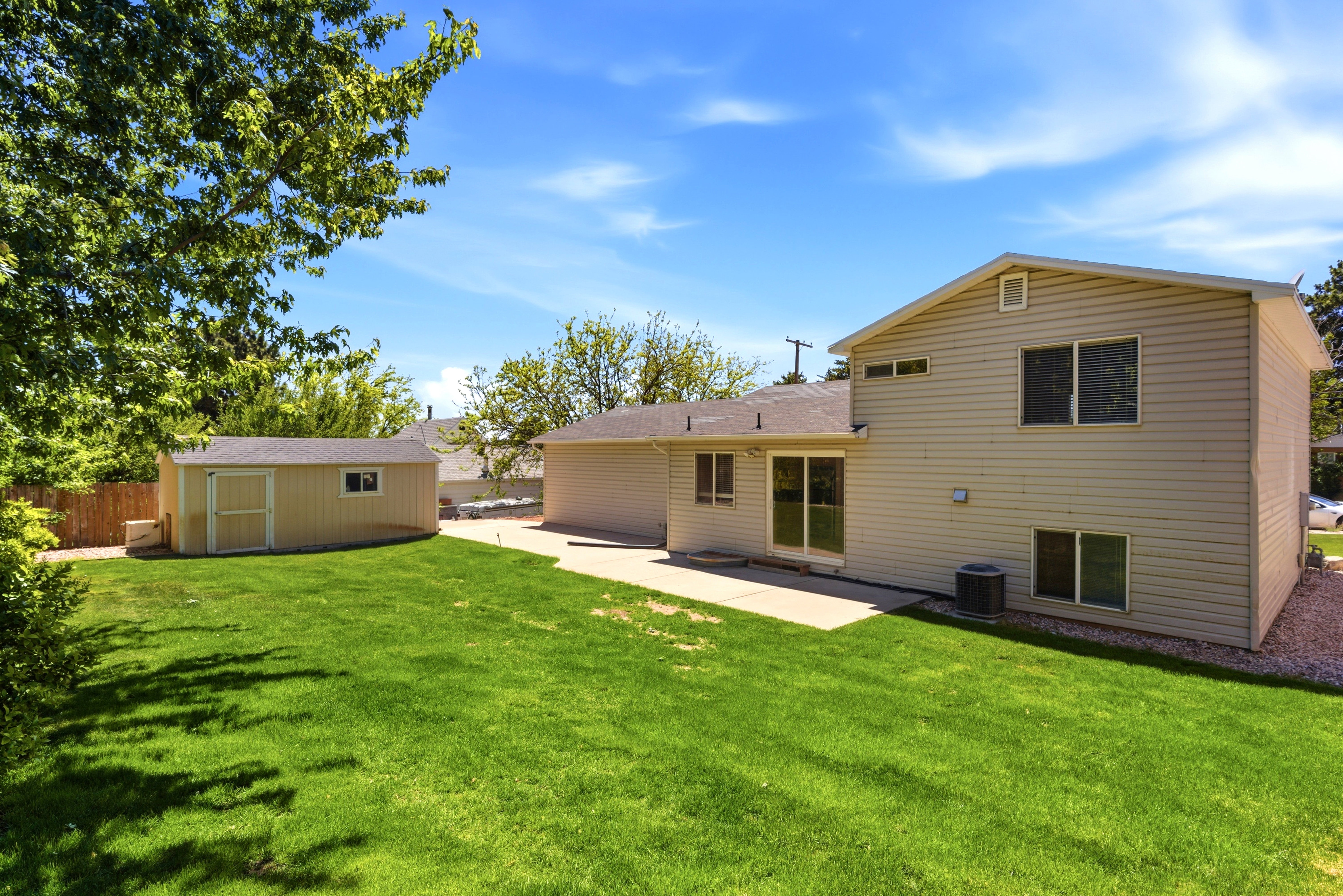 Expansive backyard featuring a lush lawn, concrete patio, and a dedicated storage shed