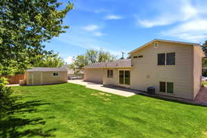 Expansive backyard featuring a lush lawn, concrete patio, and a dedicated storage shed