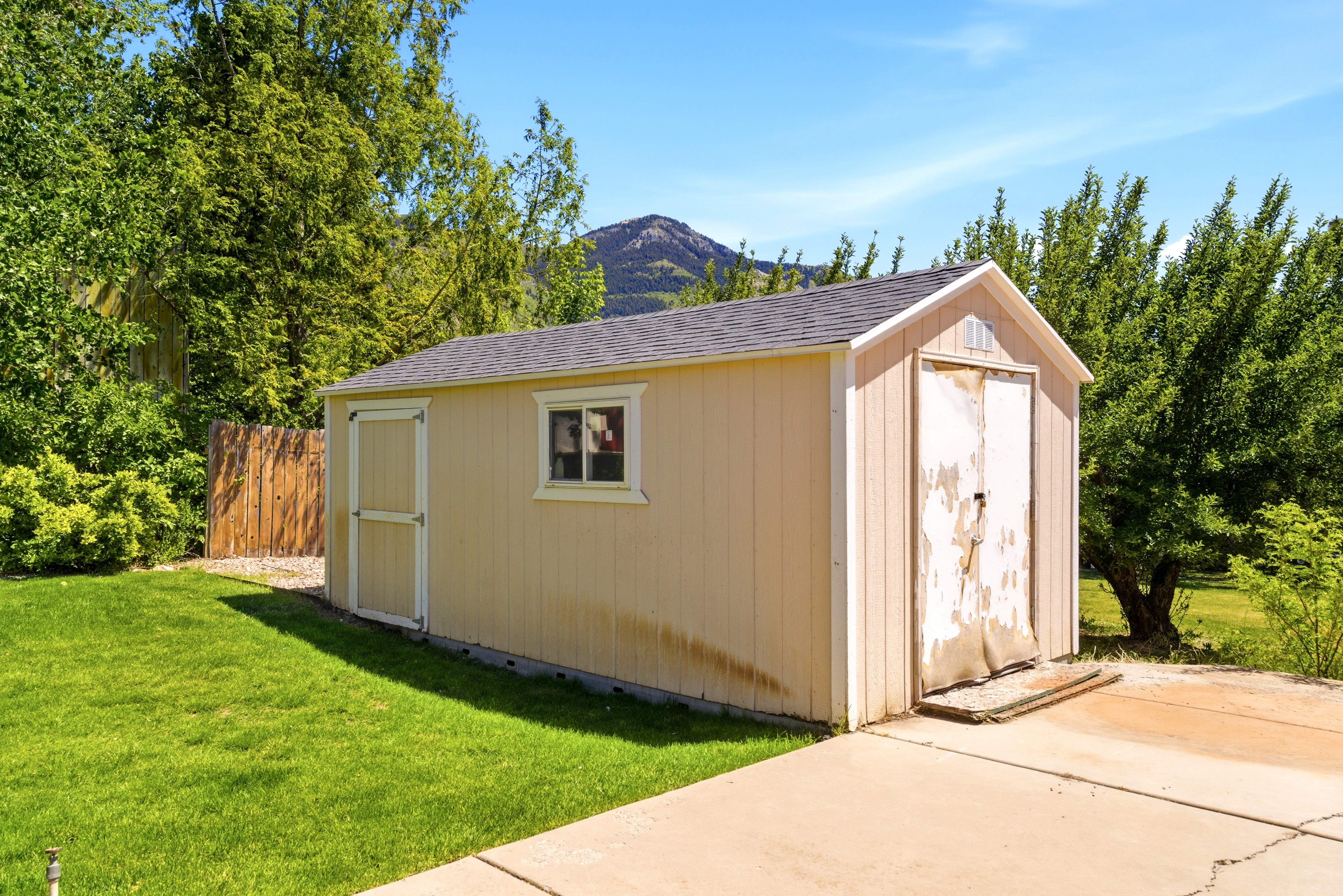 Detached utility shed with a shingle roof, single window, and two entry doors, situated on a concrete slab