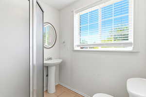 Bathroom featuring a pedestal sink, a framed oval mirror, a window with blinds, and tile flooring