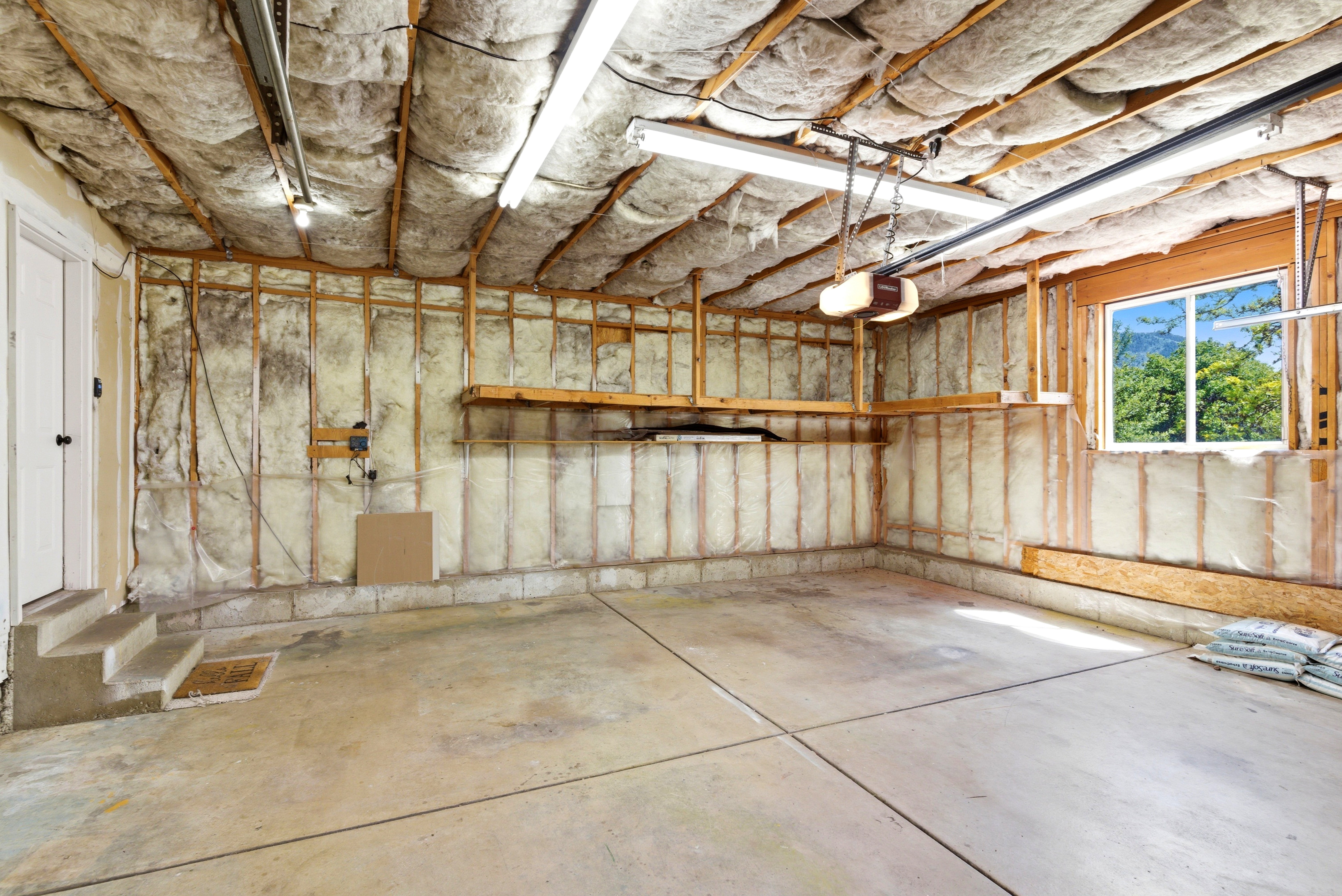 Spacious garage with concrete flooring, exposed insulation, a window, built-in shelving, and a garage door opener mechanism