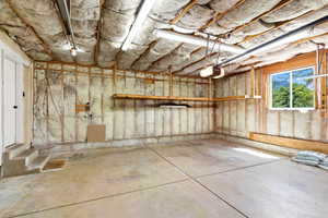Spacious garage with concrete flooring, exposed insulation, a window, built-in shelving, and a garage door opener mechanism