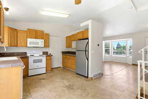 Kitchen featuring wood-finish cabinetry, white appliances, and light-toned tile flooring