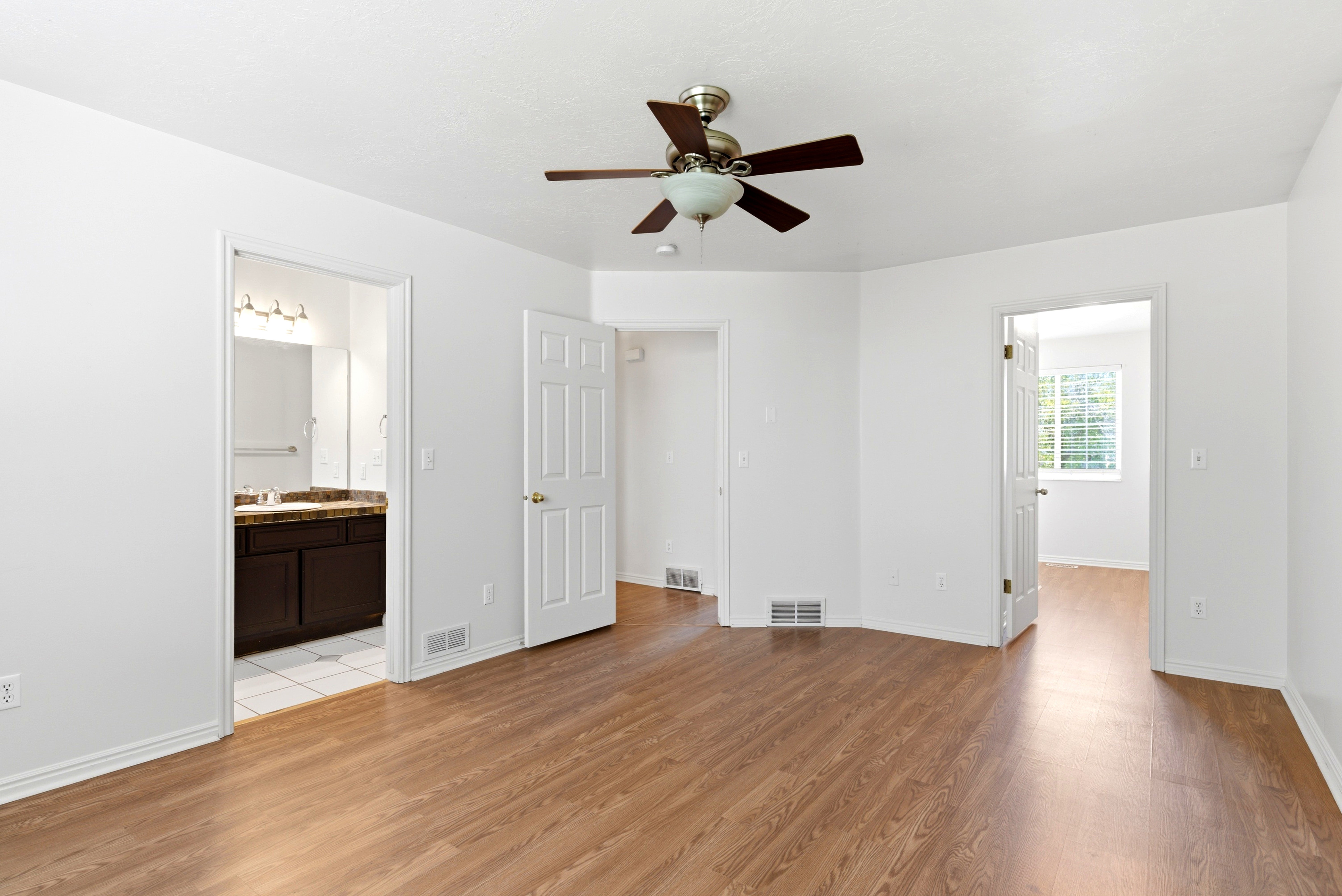 Spacious room featuring wood-finish flooring, a ceiling fan with integrated lighting, and white walls