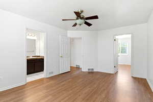 Spacious room featuring wood-finish flooring, a ceiling fan with integrated lighting, and white walls