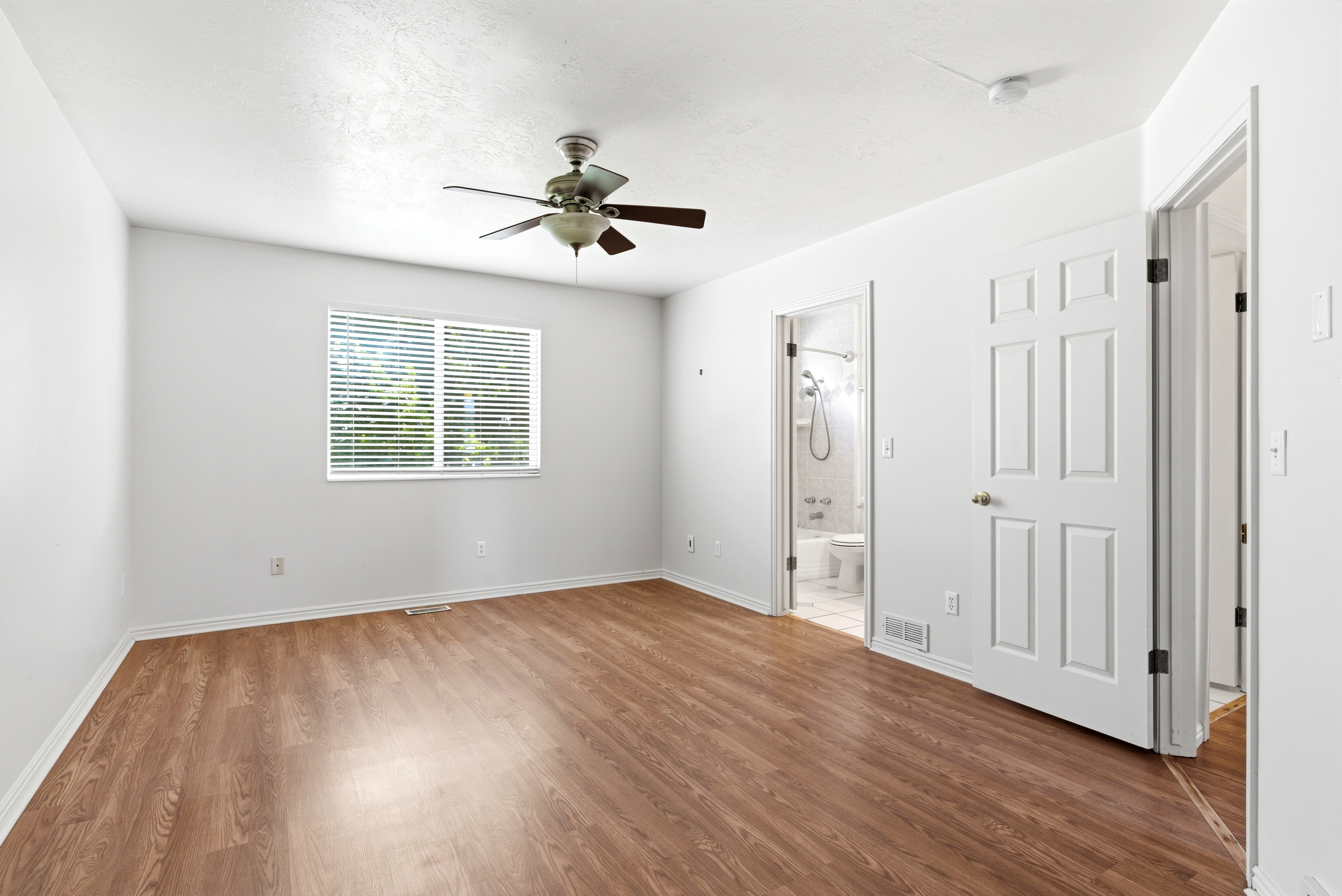 Spacious room featuring wood-finish flooring, a ceiling fan, and a window with horizontal blinds