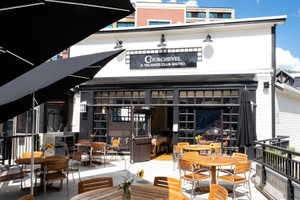 Outdoor patio featuring multiple circular wood-top tables with matching chairs, black market umbrellas, and a black metal railing