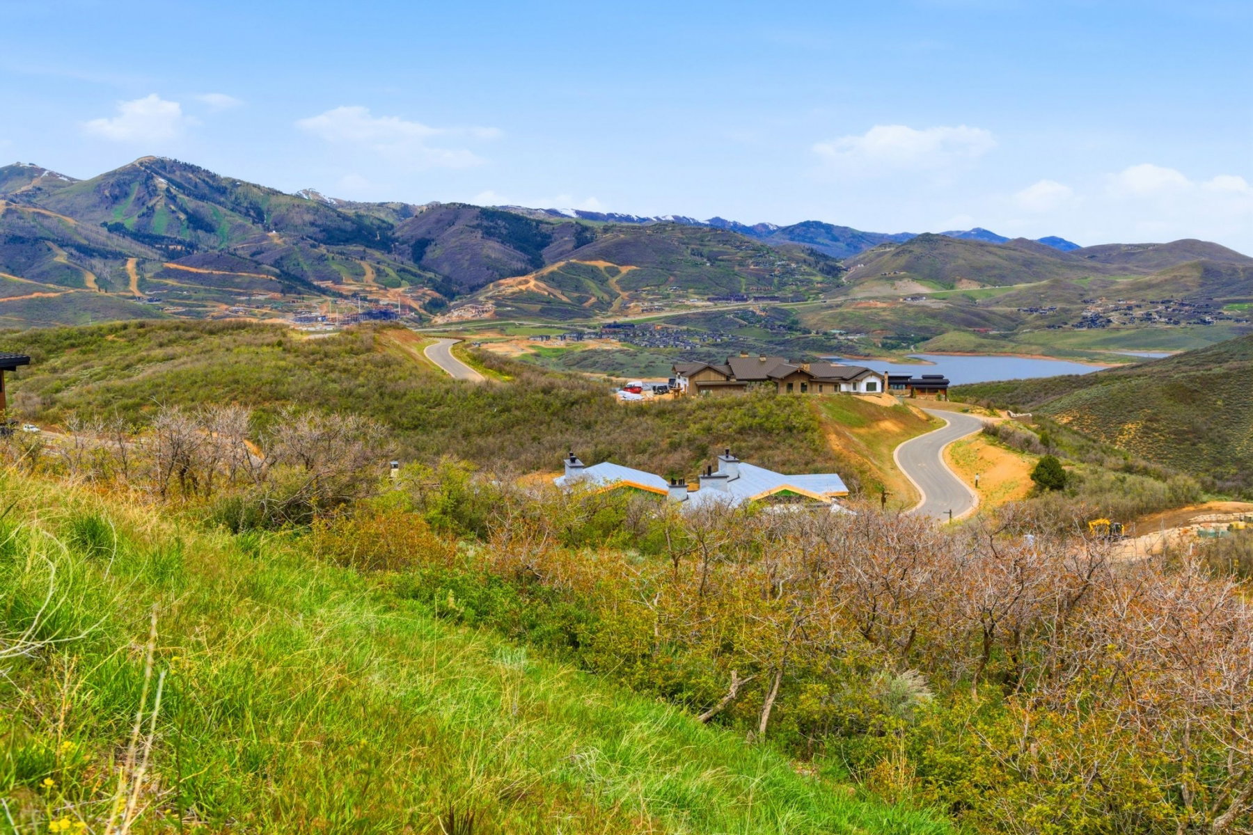 Expansive mountain landscape featuring a lake, winding roads, and residential structures