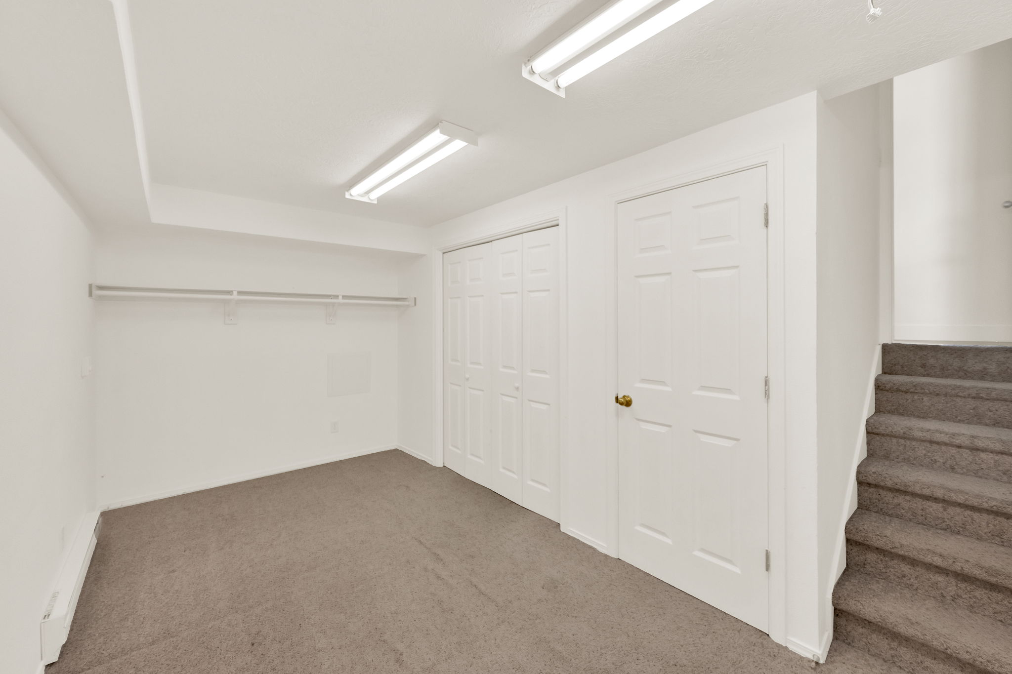 Carpeted room with white walls, two fluorescent ceiling light fixtures, built-in shelving, and bifold closet doors