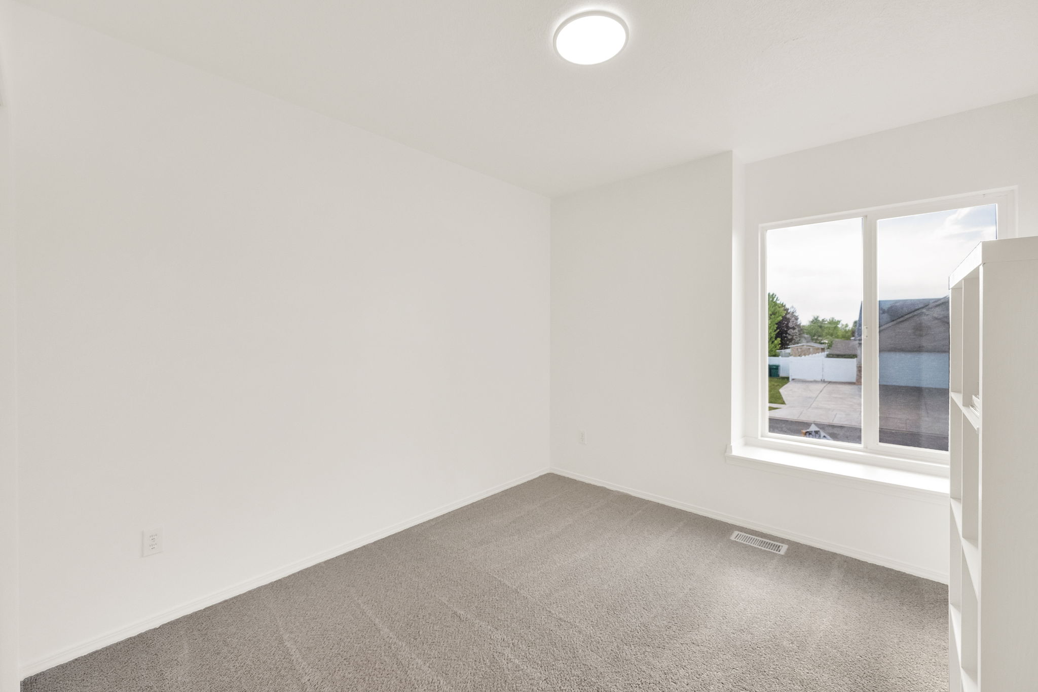 Bright room featuring light gray carpet flooring, white walls, and a large window with white framing