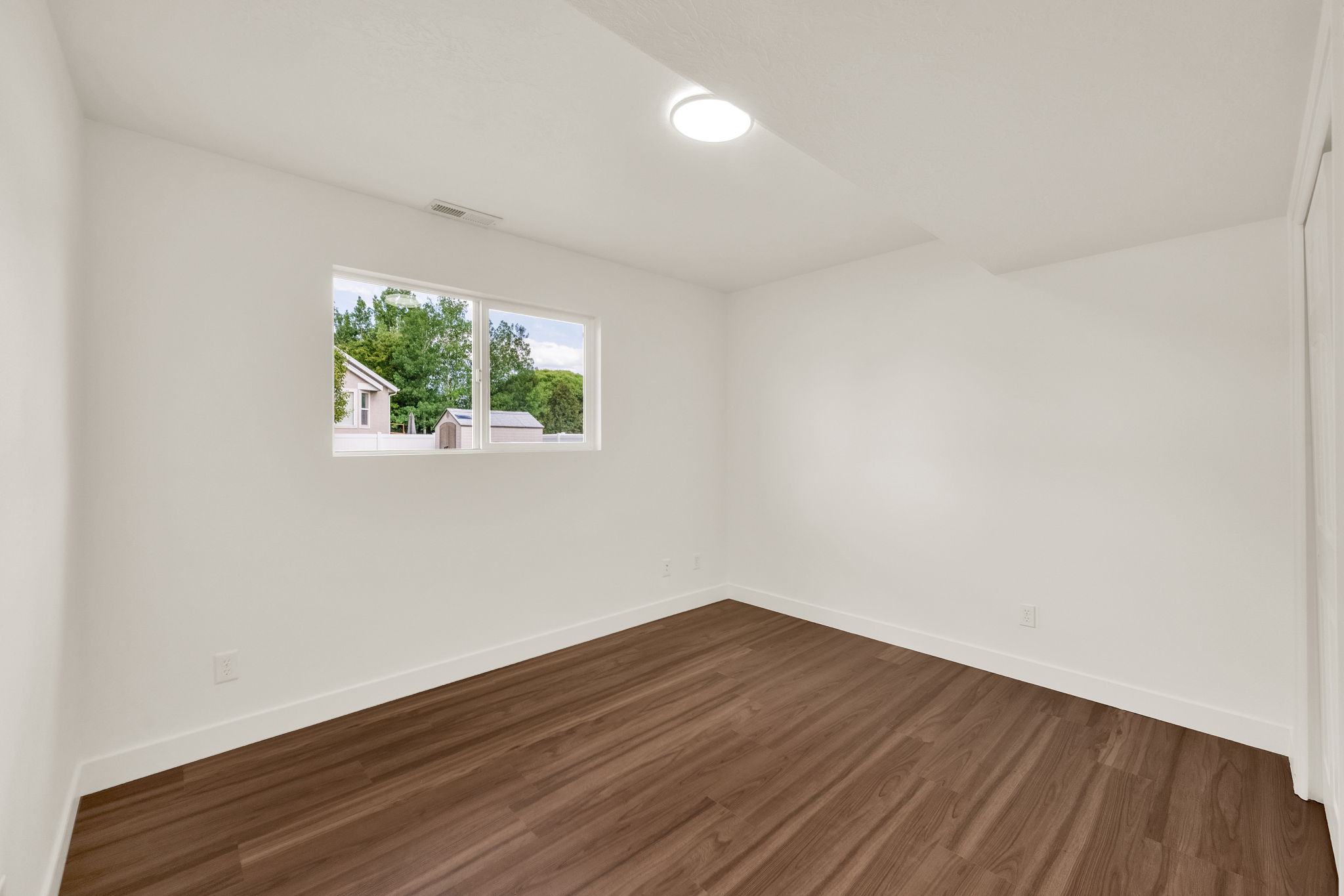 Room featuring wood-finish flooring, white walls, and a window with white trim