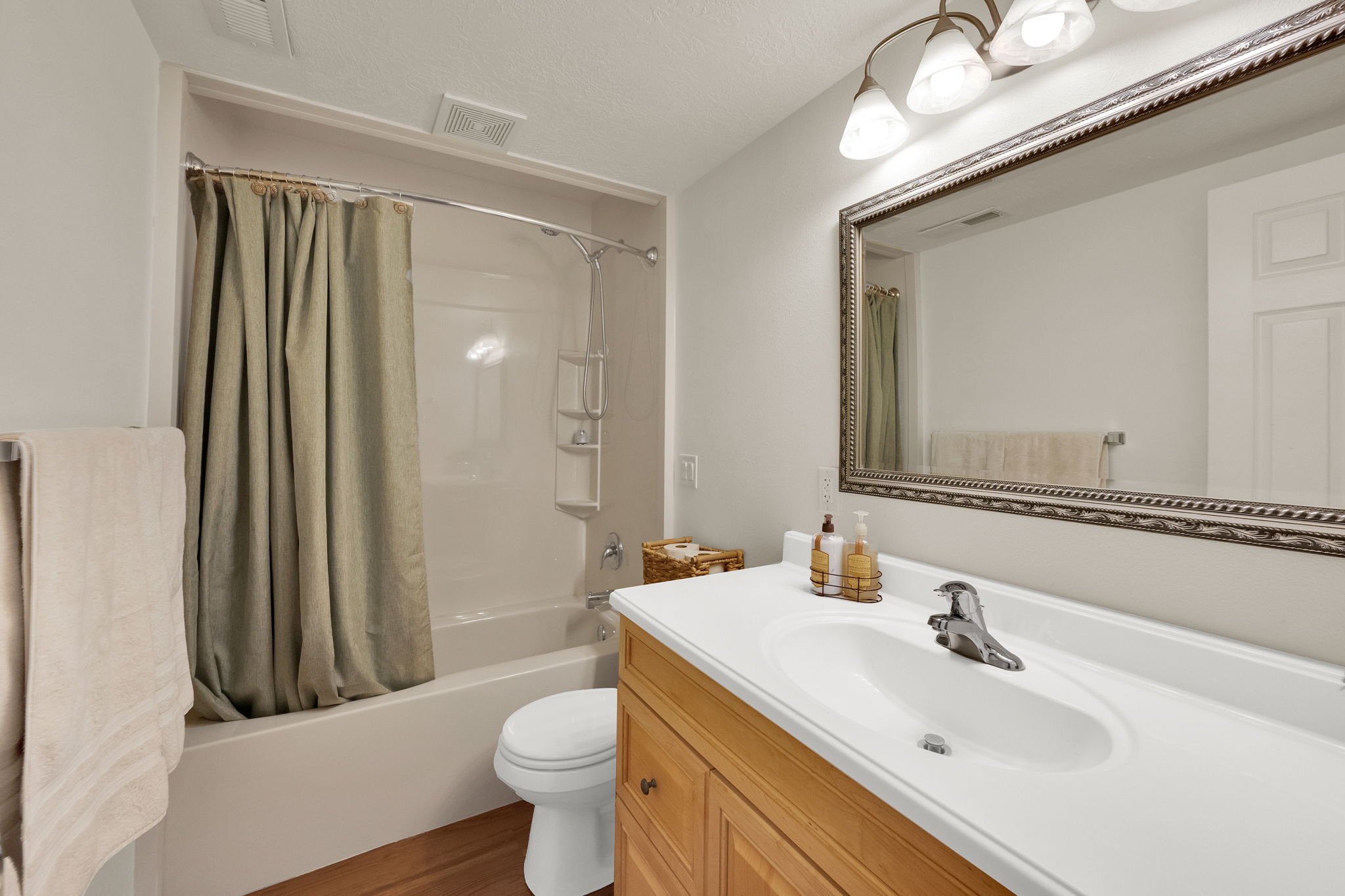 Bathroom featuring a wood-finish vanity with an integrated white sink, a decorative framed mirror, and a full bathtub with a shower kit