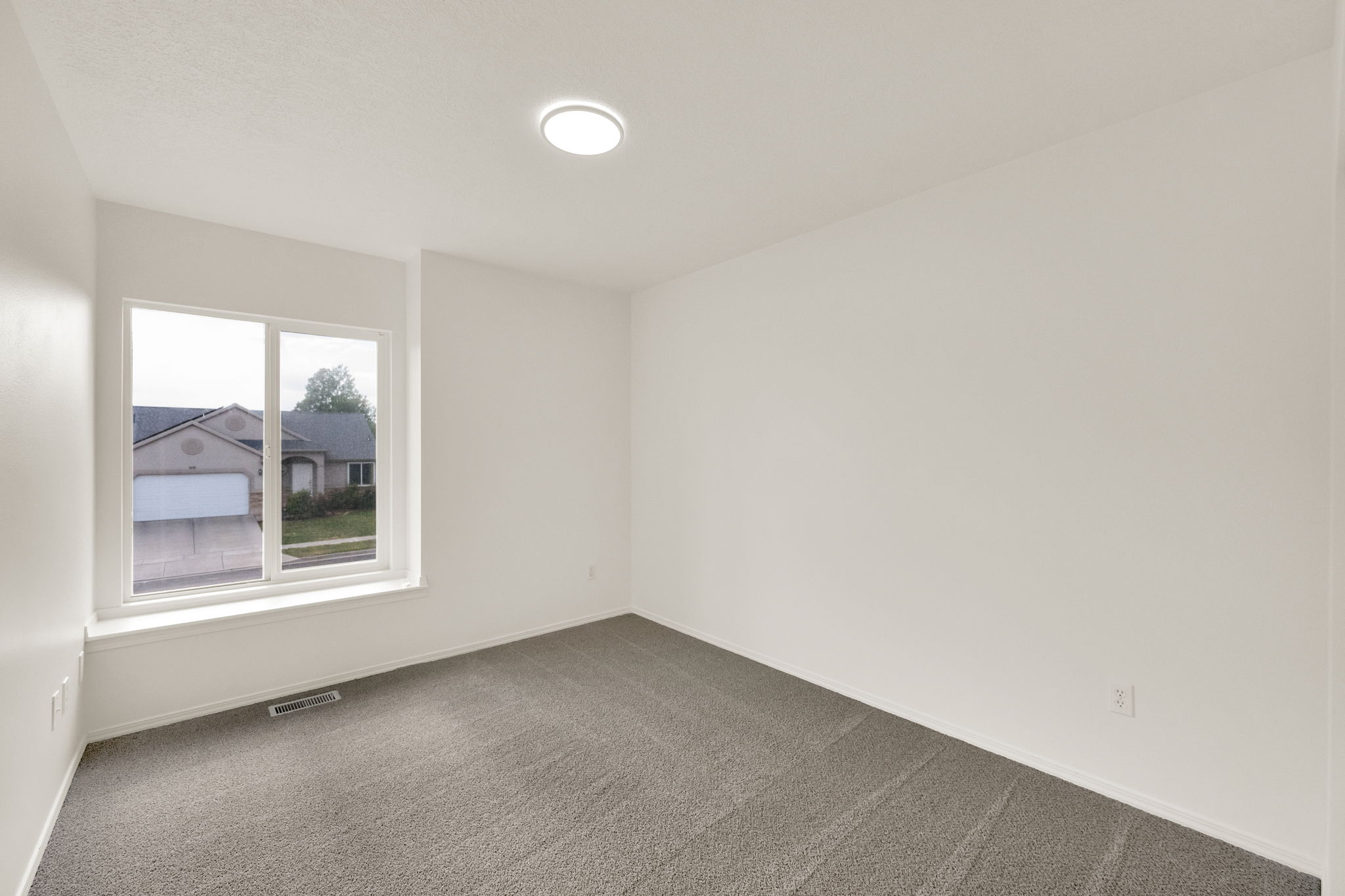 Bright interior space featuring a large window with white trim, neutral wall tones, and gray carpeting
