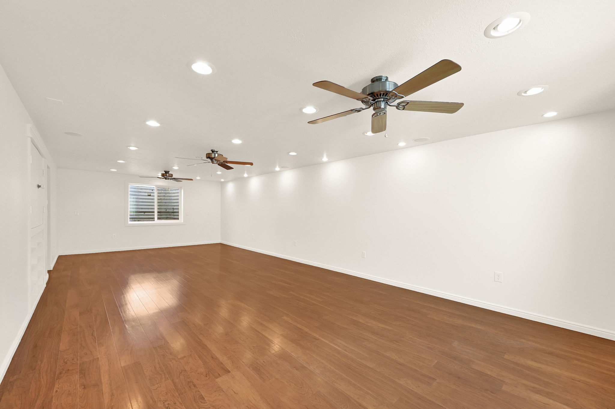 Spacious room featuring wood-finish flooring, recessed lighting, and multiple ceiling fans for air circulation