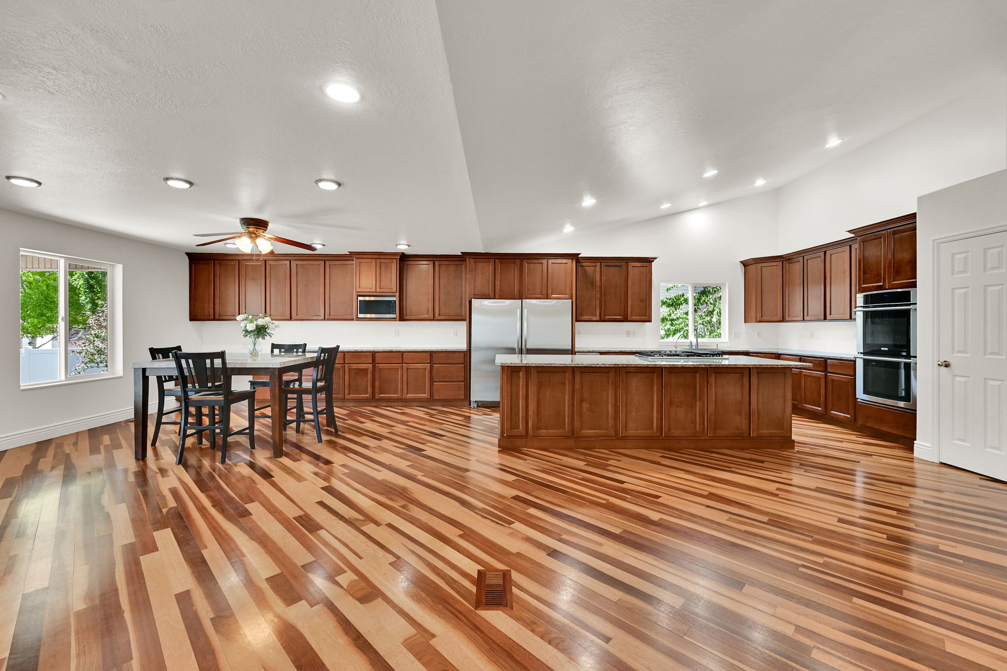 Spacious kitchen and dining area featuring vaulted ceilings, wood-finish flooring, abundant wood cabinetry, stainless steel appliances, and an expansive island