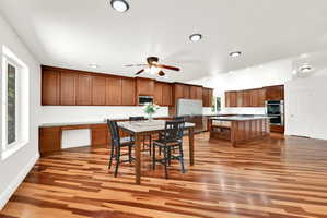Spacious kitchen featuring extensive wood cabinetry, stainless steel appliances, a large center island, and wood-finish flooring