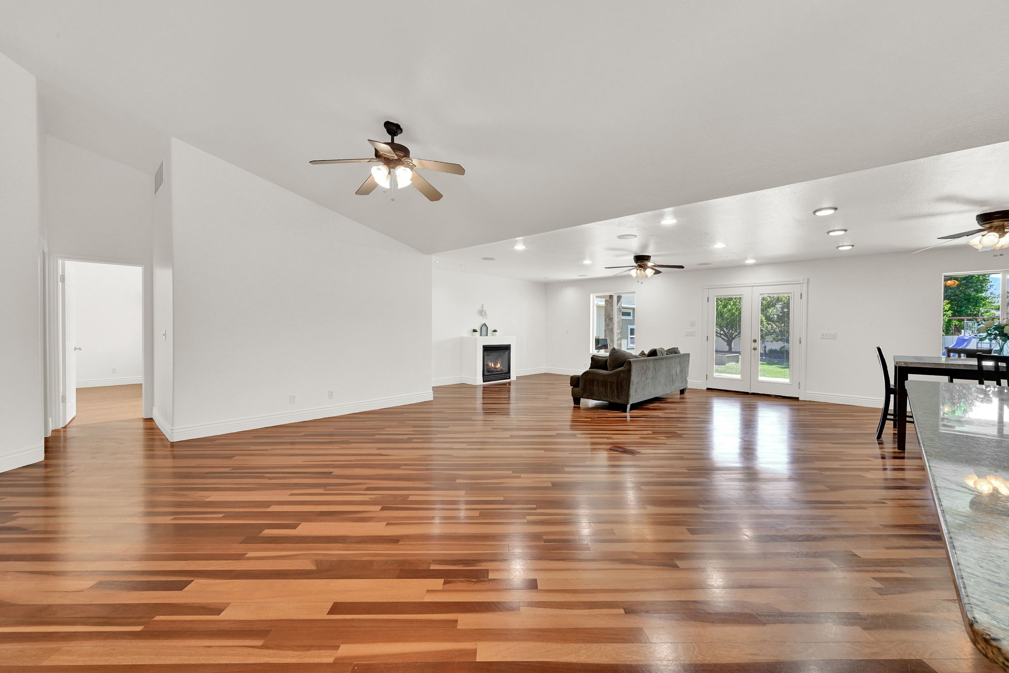 Spacious living area featuring warm wood-finish flooring, white walls, and a vaulted ceiling