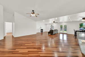 Spacious living area featuring warm wood-finish flooring, white walls, and a vaulted ceiling