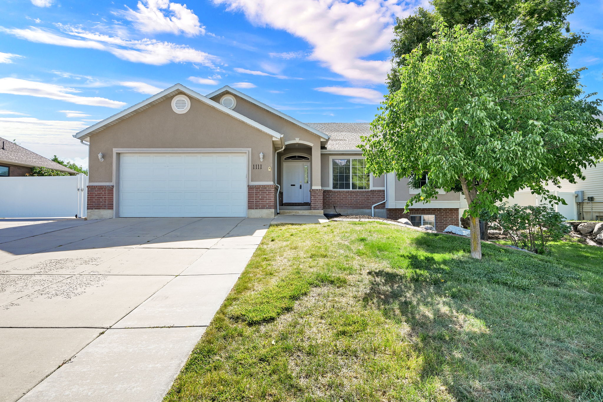 Single-story stucco residence featuring a two-car garage, brick accents, and an arched entry with a decorative sidelight