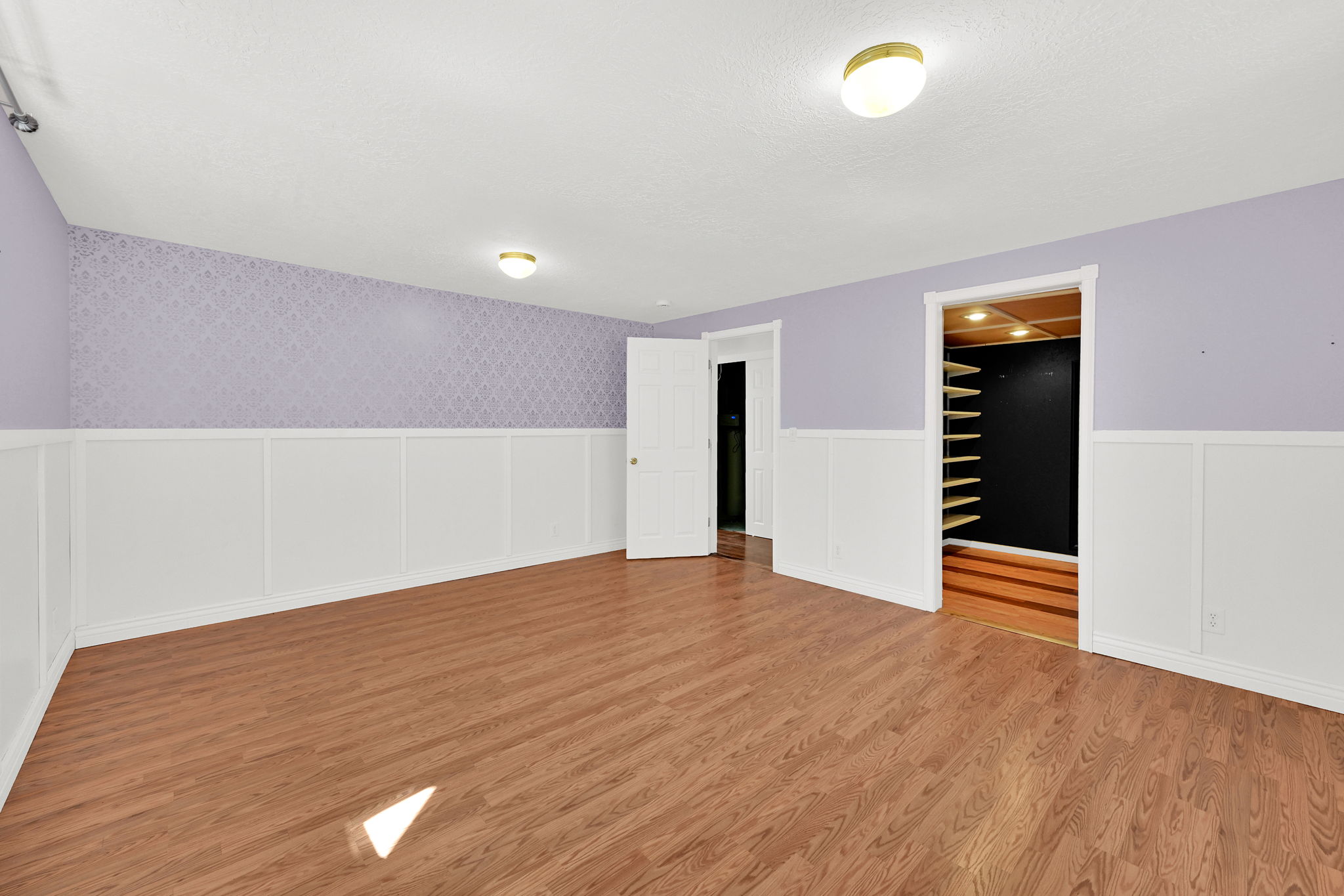 Spacious room featuring wood-finish flooring, white wainscoting, and patterned accent walls