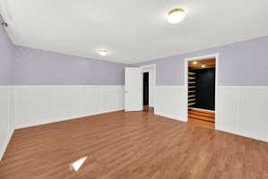 Spacious room featuring wood-finish flooring, white wainscoting, and patterned accent walls