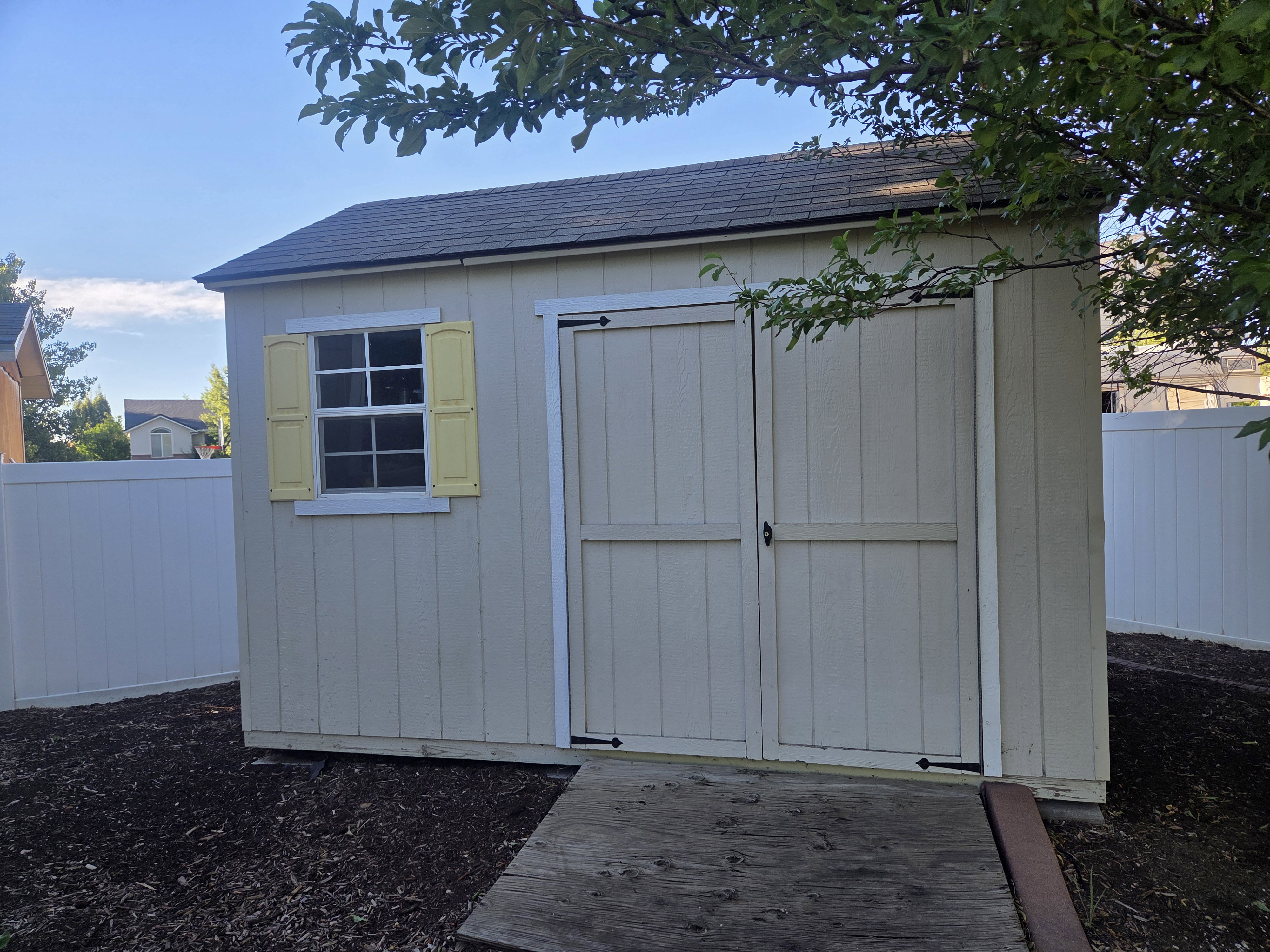Detached shed featuring a shingled roof, double barn doors, a multi-pane window with decorative yellow shutters, and a slatted wood ramp