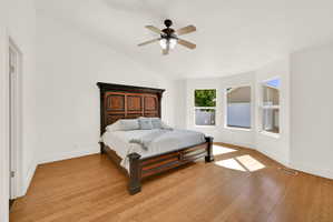 Spacious room featuring vaulted ceilings, wood-finish flooring, a ceiling fan with integrated lighting, and a bay window configuration with multiple windows