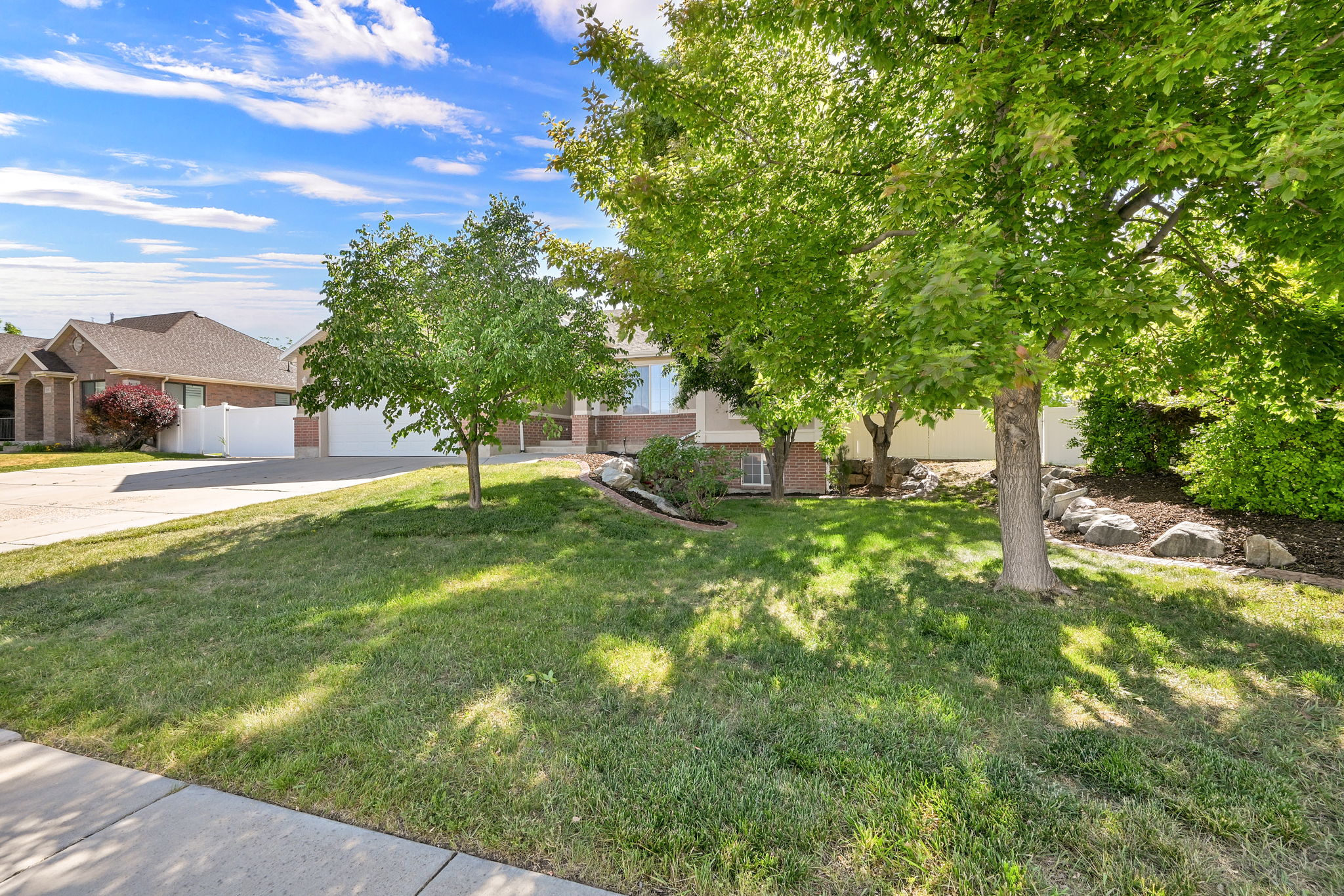 Front yard featuring mature trees, landscaped rock beds, and a manicured lawn